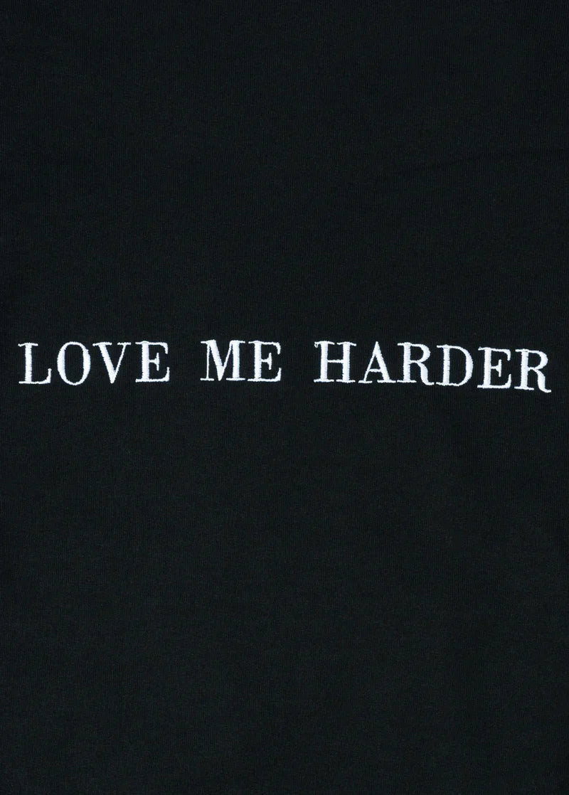 Close-up detail of Ariana Grande Love Me Harder black crewneck featuring clean white embroidered typography graphic