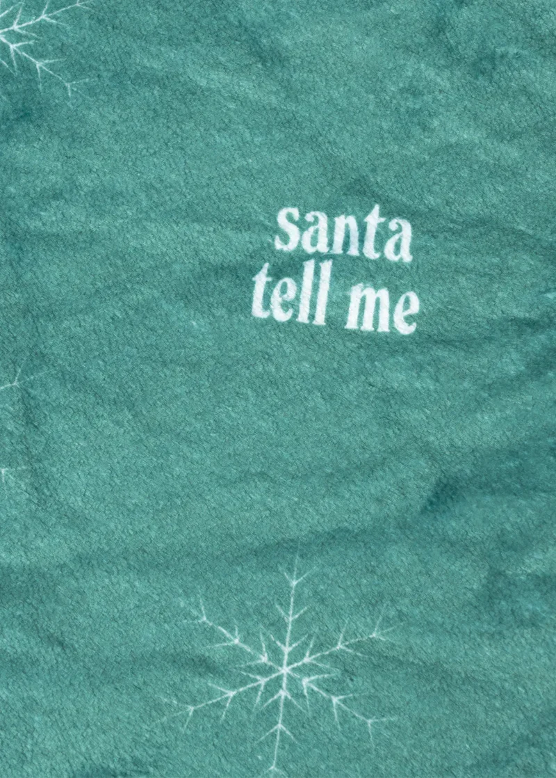 Close-up detail of Ariana Grande Santa Tell Me green fleece fabric with white snowflake holiday graphic print