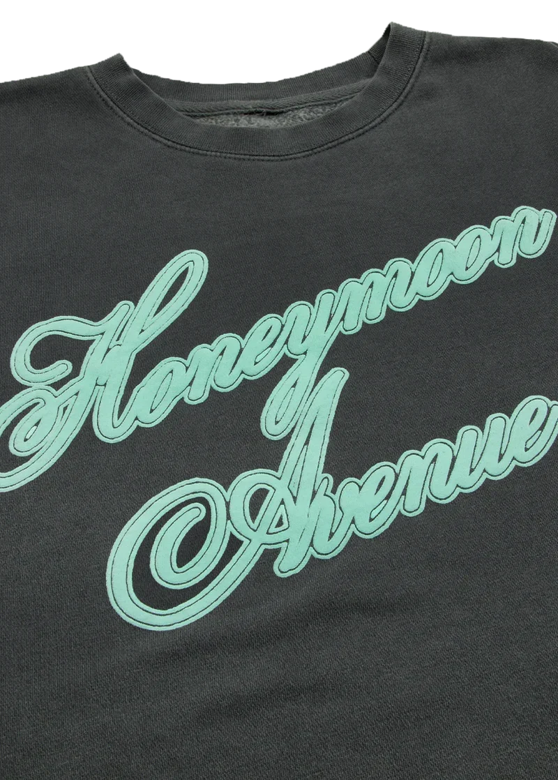 Close-up of mint Honeymoon Avenue script graphic on dark charcoal Ariana Grande crewneck
