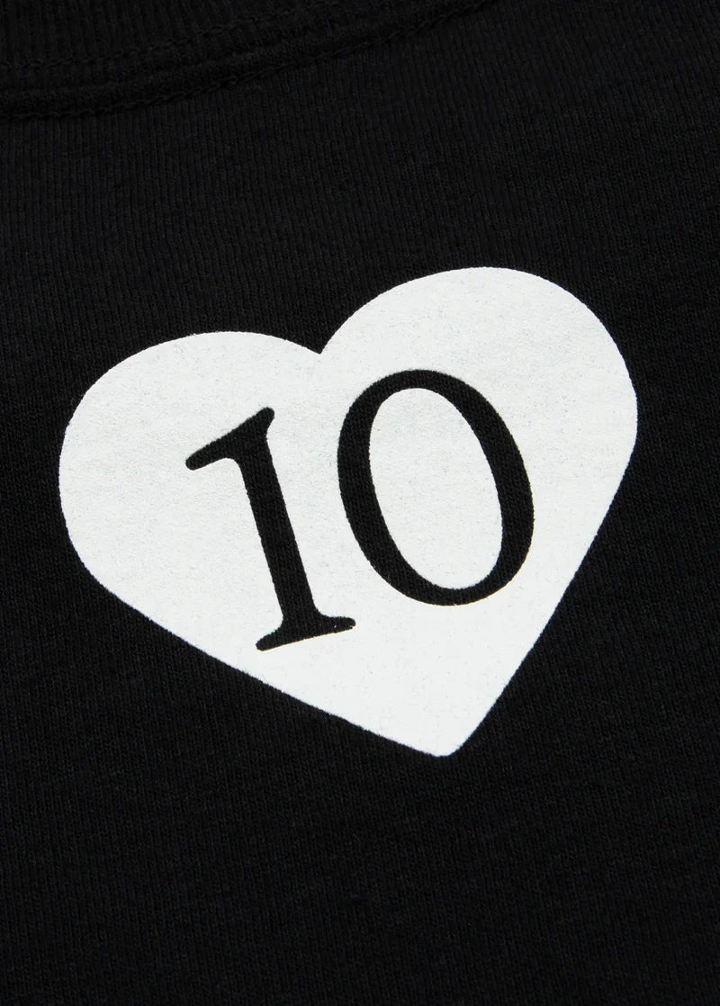 Close-up white heart 10 anniversary graphic on black Ariana Grande merch t-shirt